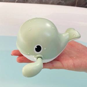 Green whale-shaped toy held in a hand with a light blue background