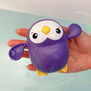 Purple bath toy shaped like a penguin held by a hand with water droplets on it.