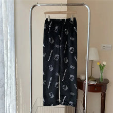 Load image into Gallery viewer, Black pants with white cat prints hanging on a rack in a room.