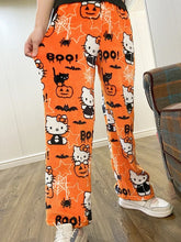 Load image into Gallery viewer, Orange Halloween-themed pants with Hello Kitty design worn by a person indoors.